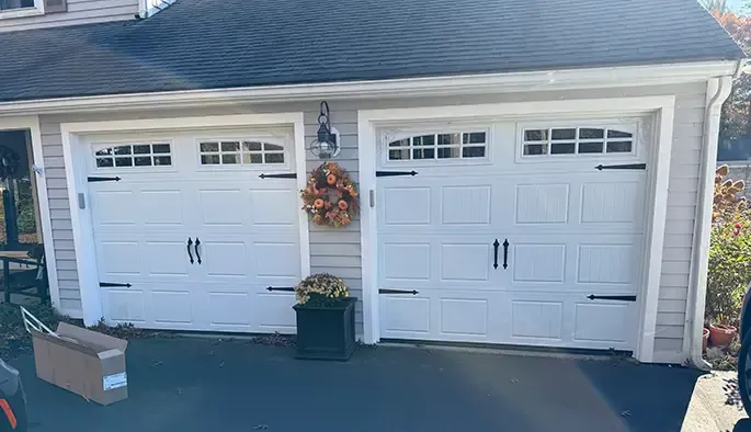 A sunny driveway with two white garage doors adorned with seasonal wreaths